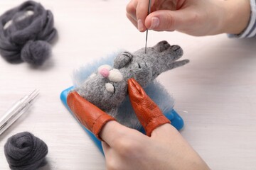 Woman felting toy cat from wool at light wooden table, closeup