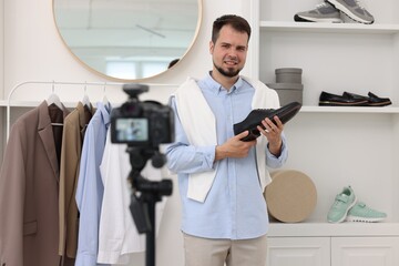 Smiling fashion blogger showing shoe while recording video at home