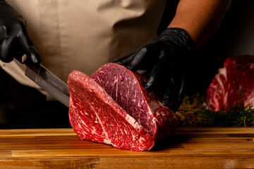 The butcher wearing black gloves cuts the meat with knife on wooden cutting board.Close-up piece of...