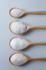 Organic white salt in spoons on light grey background, flat lay