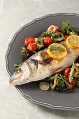 Baked fish with vegetables, rosemary and lemon on grey textured table
