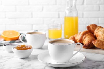Tasty breakfast. Cups of coffee, fresh croissants and jam on white marble table