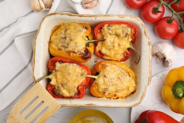 Delicious stuffed peppers in baking dish, spatula and ingredients on white textured table, flat lay