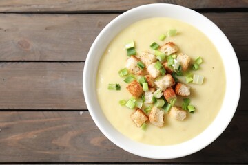 Tasty potato soup with croutons and green onion in bowl on wooden table, top view. Space for text