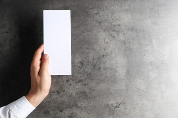 Man holding blank card at black textured table, top view. Mockup for design