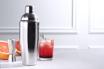 Metal shaker, delicious cocktail, jigger and grapefruit on light grey table, space for text