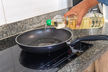 hand putting oil in a frying pan on an induction cooker