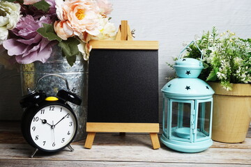 Easel mockup with blue landtern, alarm clock and flowers bouquet decoration on wooden background