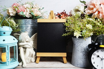Easel mockup with blue landtern, alarm clock and flowers bouquet decoration on wooden background