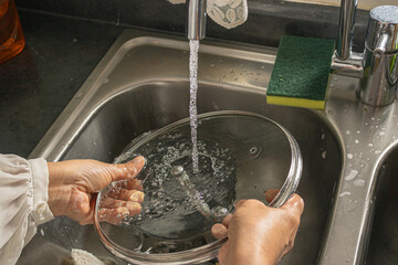 Closeup of woman washing glass lid in sink with soap and water in kitchen, top view.