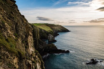 Scenic view of cliffs in Irish coast with green hills at sunset.