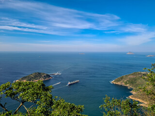 Cargo ship sailing in blue sea near island and rocky coast