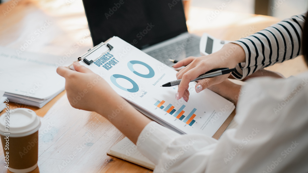 Poster hands of a professional examining a detailed business report with charts and graphs, alongside a lap