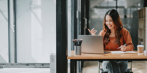 Enthusiastic young businesswoman engaging in a video call meeting with colleagues on her laptop in an office setting.