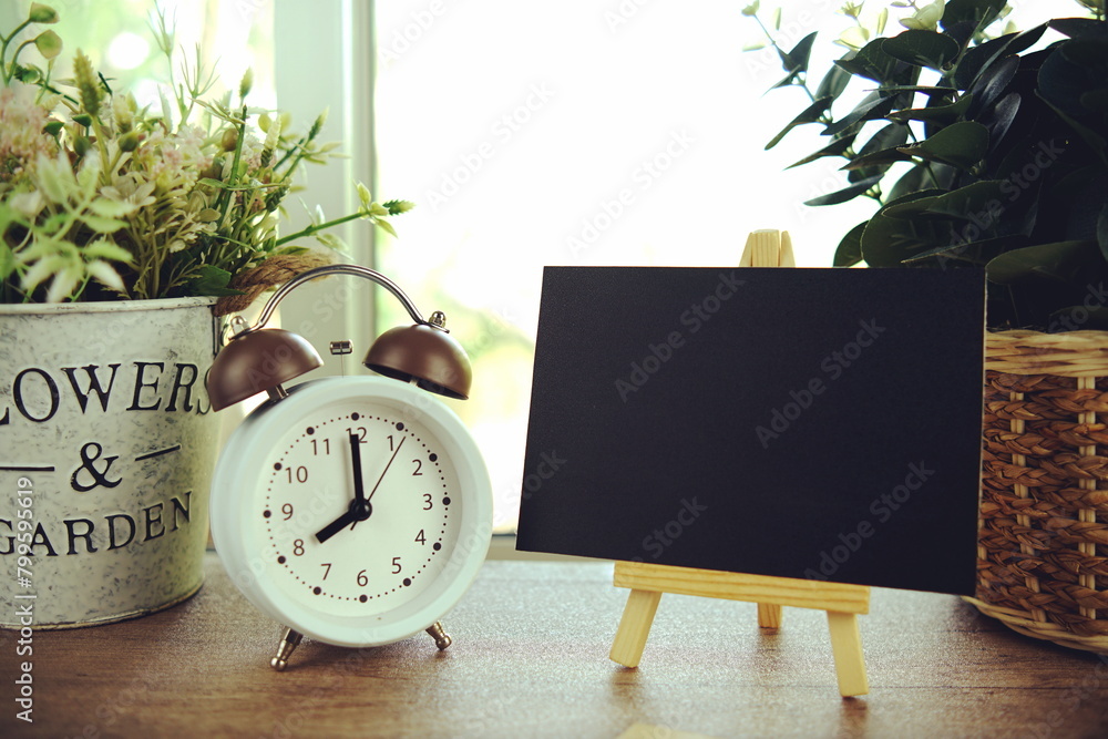 Poster empty card space for text message with wooden easel and alarm clcok on wooden background