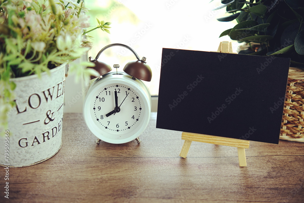 Poster empty card space for text message with wooden easel and alarm clcok on wooden background