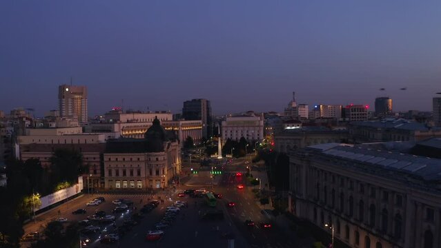 4k Drone footage. Evening in the city of Bachares, the capital of Romania. A flock birds fly across the foreground against the backdrop of burning city lights after sunset. Traffic on the streets