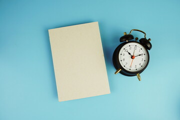 Black alarm clock with empty paper card top view on blue background