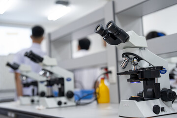 A man is standing behind a desk with two microscopes on it