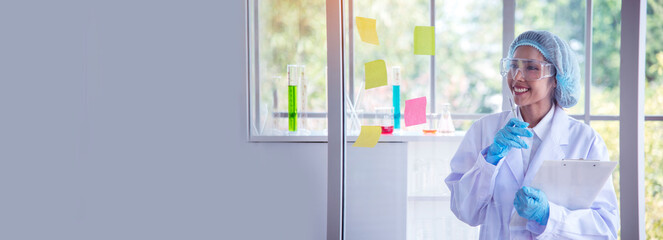 Fototapeta premium Banner Asian woman scientist hand write note research in medical lab look at science microscope. Panorama biology chemistry lab. Asian Female technician laboratory using microscope with copy space