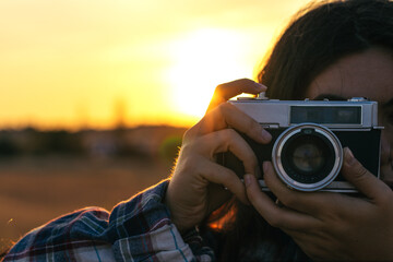 Young woman taking photos with analog camera in the field at sunset