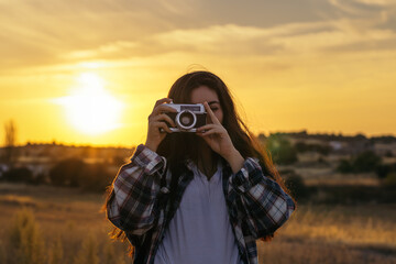 Young woman taking photos with analog camera in the field at sunset