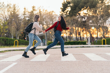 two student girls crossing crosswalk holding her hands, running and smiling