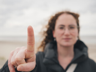 Close-Up of Finger Gesture with Blurred Woman and Beach