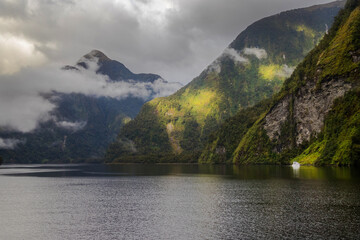 Seascape in Doubtful Sound Fiord, New Zealand, green costline and reflection in a wather, cloudy...