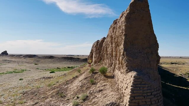 A boy at the Turkestan walls of the ancient city of Sauran on a sunny day against a blue sky. Ancient buildings, fortress, ruins, architecture in the settlement of Sauran. Archaeological excavations.