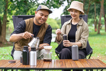 Happy asian couple clinking coffee mug together at camp side, They feeling relaxed and refreshing while camping in the nature. Recreation and journey outdoor activity lifestyle.	