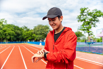 Athletic young asian man press the button of smart watch for checking heart rate, distance,...
