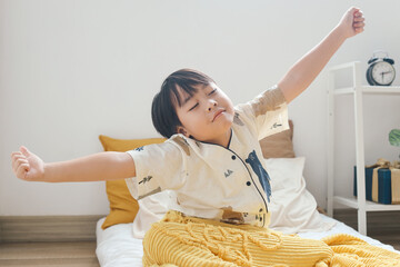 Cute little kid boy in pajamas wake up in the morning, stretching hand rise up to the air while...