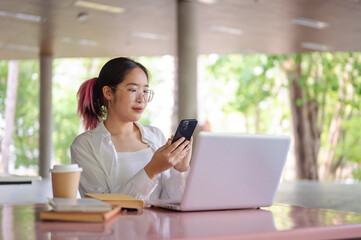Obraz premium A female college student using her smartphone while sitting at a table in a campus cafeteria.