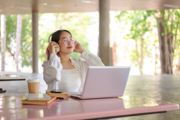 A happy Asian female college student is enjoying music on her headphones in her campus cafeteria.