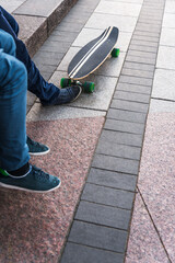 Two Teenage Skateboarders Sit In The City Square With Their Skateboard. Legs With A Skateboard