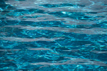 Water background. Blue water, ripples and highlights. Texture of water surface and tiled bottom.
