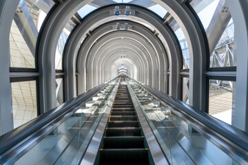 View from the bottom of a single upwards moving escalator surrounded by steel and glass arches 