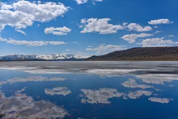Mountain lake in spring in sunny weather, the sky with clouds is reflected in the water.
