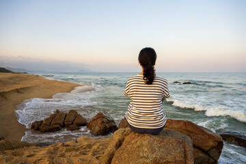 A woman sitting at beach and looking to sunrise.