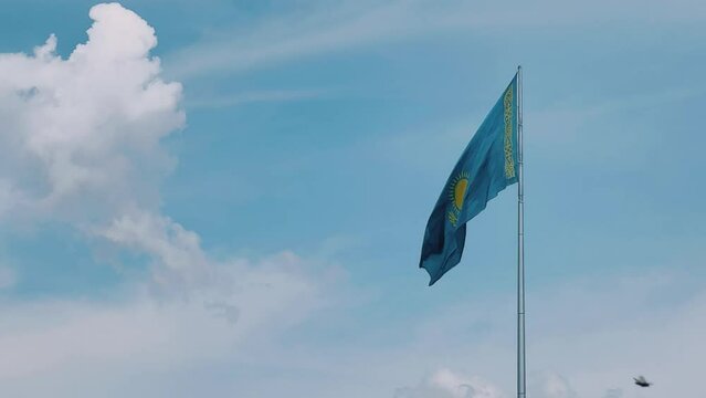The flag of Kazakhstan is flying in the wind. Astana - Nur Sultan. A waving flag on a flagpole against the blue sky in Kazakhstan. The flagpole of the Republic of Kazakhstan on a bright sunny day. 4K 