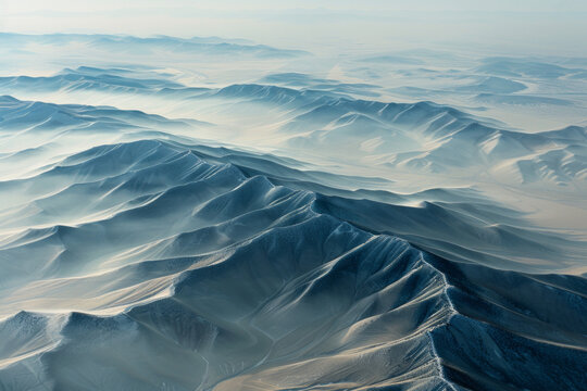 Aerial view of layered patterns of mountain ridges receding into the distance, with their alternating light and shadow creating a minimalist composition.
