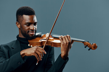 Talented young African American man playing melodious music on violin against a neutral gray...