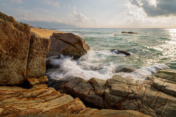 Long exposure photo of waves and rocks at sunrise.