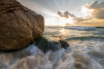 Long exposure photo of waves and rocks at sunrise.