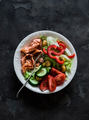 Delicious balanced lunch - grilled salmon, boiled egg, fresh vegetable salad on a dark background, top view
