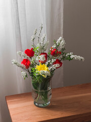 A spring bouquet of red tulips and spirea in a glass vase on a wooden bench