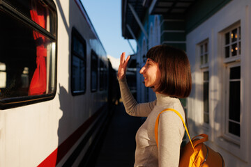 young traveler stands on the platform and says goodbye, waving to someone on the train. say goodbye...