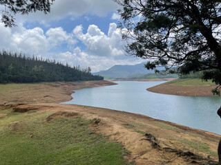 Towering mountains, river with visible small island, blue and white sky, reflection visible in water, nature's gift of greenery everywhere is the way