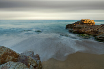 Long exposure photo of waves and rocks on an overcast day.
